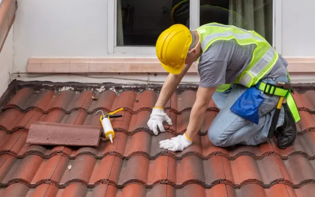 Beton kiremit üzerinde diz çökmüş usta silikonla sızdırmazlık tamiri yapıyor