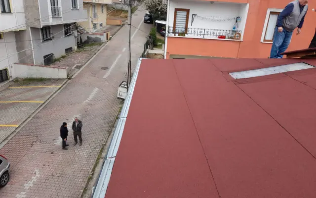 Bordo membran kaplı çatı kenarında oluk ve ayakta duran usta