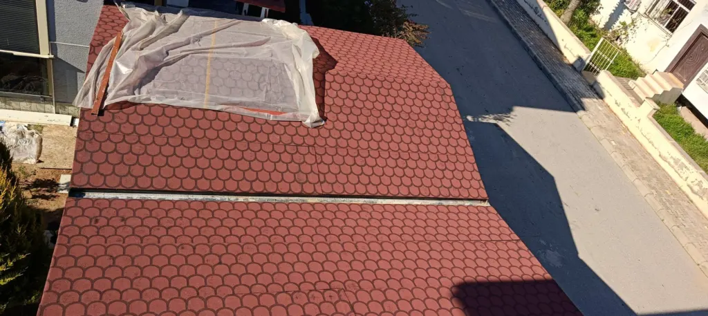 Kırmızı oval shingle kaplı çatıda mahya bölümü naylon örtüyle korunuyor