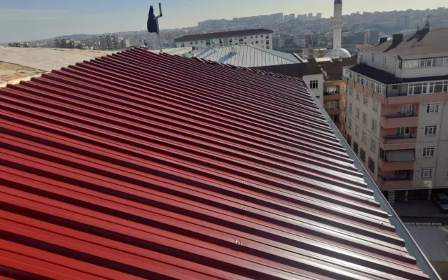 Şehir manzarası eşliğinde kırmızı trapez sac kaplanmış eğimli çatı yüzeyi